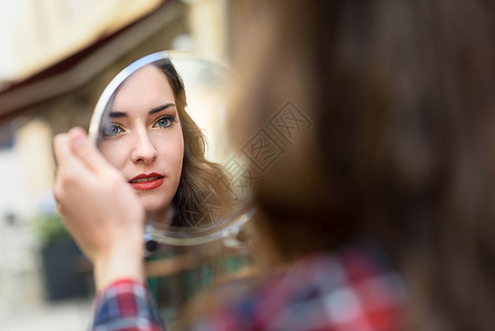 轻女人城市背景中的小镜子里看自己的肖像背景图片