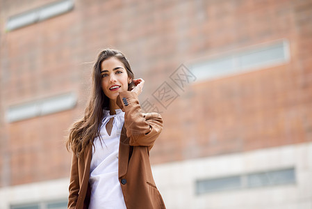 棕色上衣的女孩轻的女人,留着漂亮的头发站办公楼外穿正式服装的女商人,留着波浪式发型穿着棕色夹克裤子的轻女孩背景