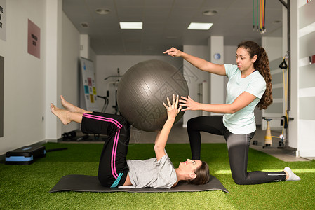 物理治疗师协助轻的白种人妇女医院健身房康复期间用瑜伽球锻炼女理疗师理疗中心培训名病人健康高清图片素材