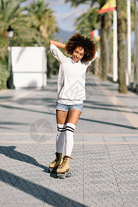 微笑的黑人妇女溜冰鞋骑户外海滩长廊与棕榈树阳光明媚的日子里,带着AFRO发型的微笑女孩穿着溜冰鞋的黑人女人海滩长廊背景图片