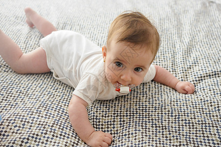 快乐的女婴,四个月大,床上用奶嘴图片