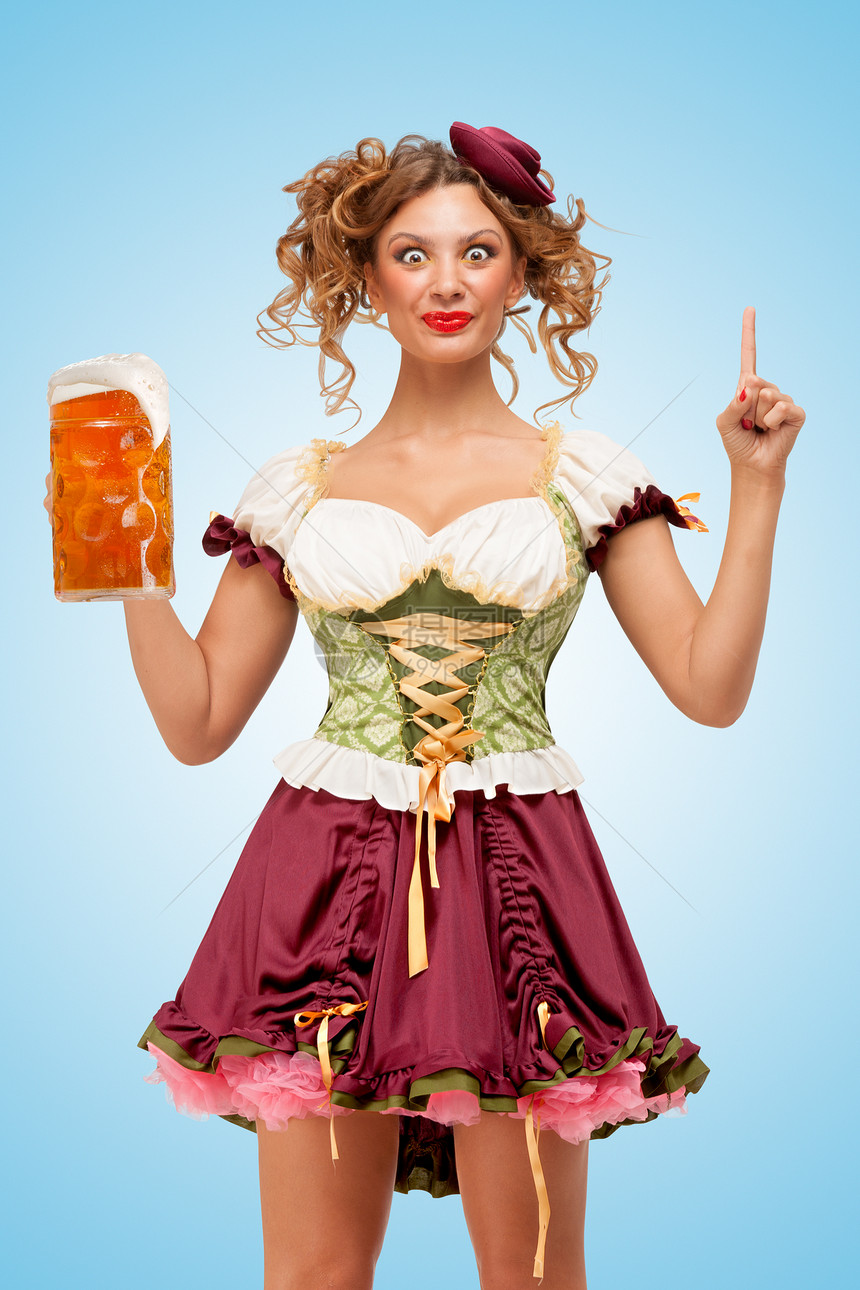 轻感的啤酒节女服务员穿着传统的巴伐利亚连衣裙,戴着个啤酒杯,蓝色背景上个想法图片