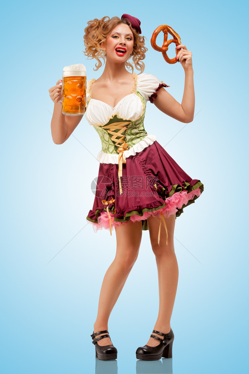 轻感的啤酒节女服务员穿着传统的巴伐利亚连衣裙,着个椒盐卷饼啤酒杯,蓝色的背景下开心地笑着图片