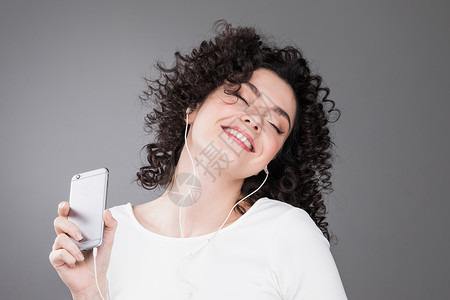 女人听音乐灰色背景的耳机中拍摄快乐女听音乐的肖像图片