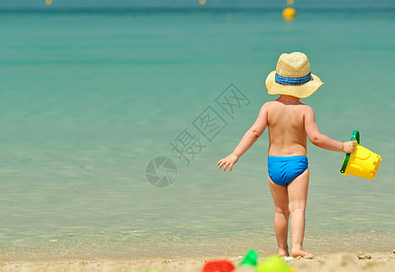 海洋塑料两岁的蹒跚学步的男孩海滩上玩海滩玩具背景