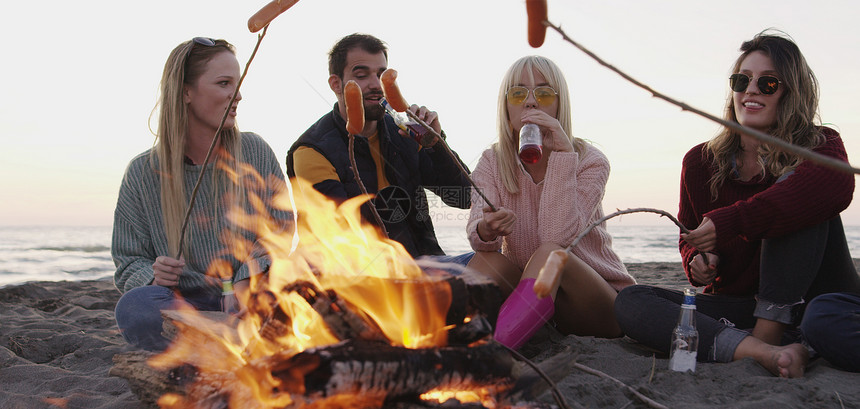 群轻的朋友深夜坐炉火旁,烤香肠,喝啤酒,聊天,玩得开心图片
