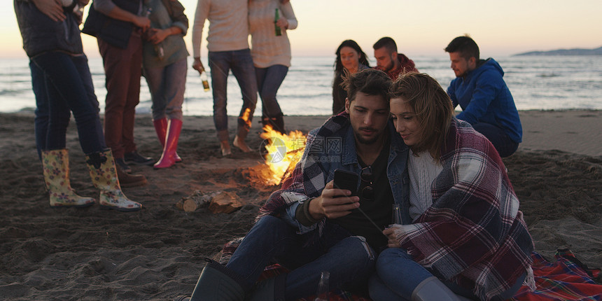 夫妇海滩聚会上用手机朋友喝啤酒,玩得开心图片