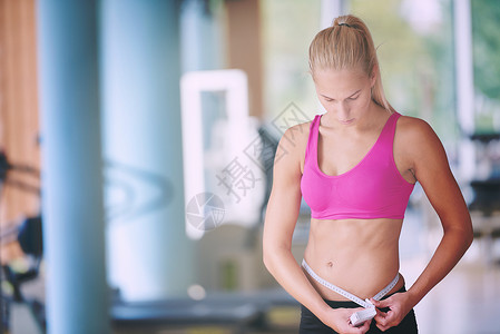 轻健康的女人健身馆的训练中测量腹部轻健康的女人测量腹部图片