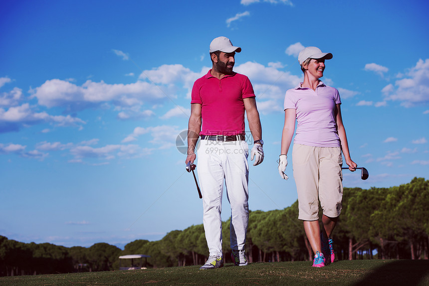 轻夫妇步行高尔夫球场的下个洞带高尔夫球袋的人夫妇高尔夫球场散步图片