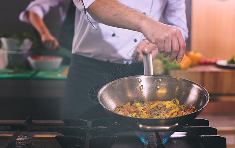 轻的男厨师商业厨房把香料放炒菜上厨师炒菜上放香料图片