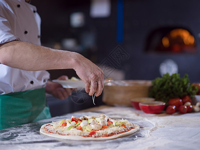 厨师把新鲜蔬菜放厨房桌子上的比萨饼上厨师把新鲜蔬菜放比萨饼上图片
