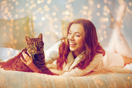 笑着的猫宠物,舒适,休息人的快乐的轻女人猫躺床上家快乐的轻女人,猫躺家里的床上背景