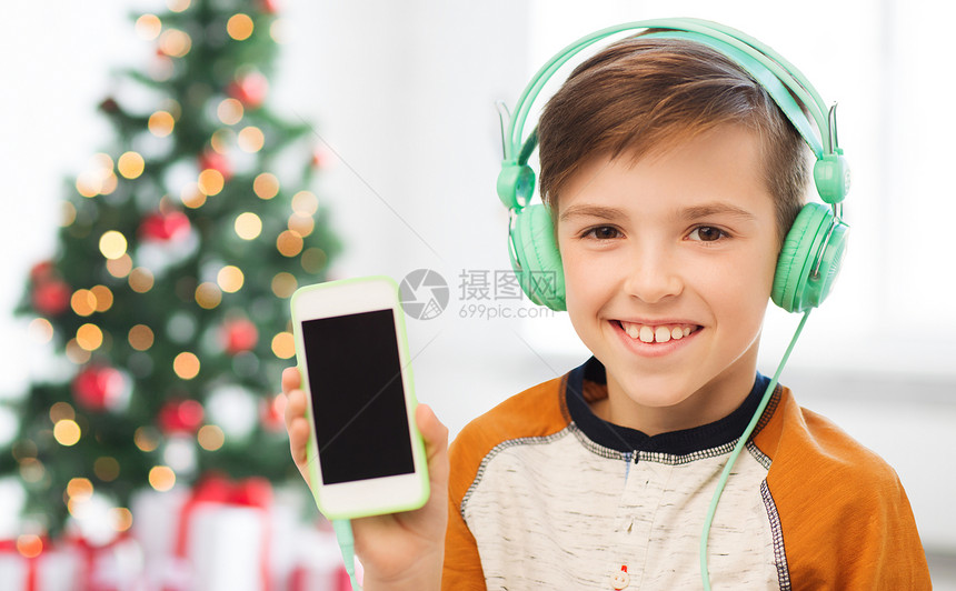 孩子,技术人的微笑男孩与智能手机耳机听音乐家里的诞树背景诞节带着智能手机耳机的男孩图片