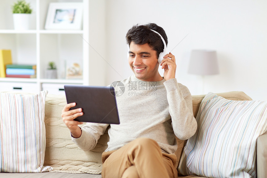 技术,休闲人的快乐的人无线耳机与平板电脑家里听音乐男人手机与平板电脑听音乐图片