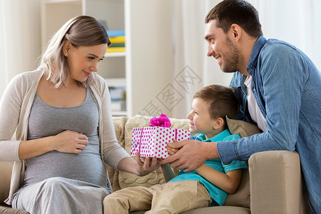 家庭,节日问候的父亲小儿子送礼物给幸福的怀孕母亲家家里给怀孕母亲送礼物成人高清图片素材