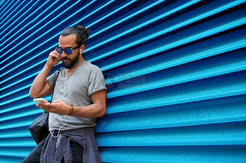 人,技术,旅游旅游男人带着耳机,智能手机袋子城市街道上,听音乐带肋的蓝色墙壁背景墙上戴着耳机智能手机的男人图片
