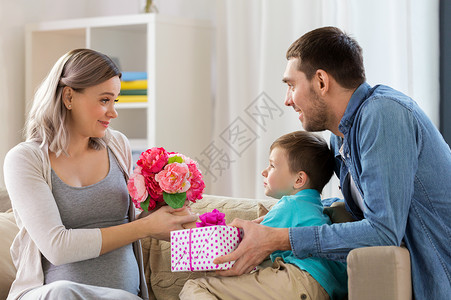 男人送礼物家庭节日问候的父亲小儿子家里送花礼物给幸福的怀孕母亲家里给怀孕母亲送礼物背景