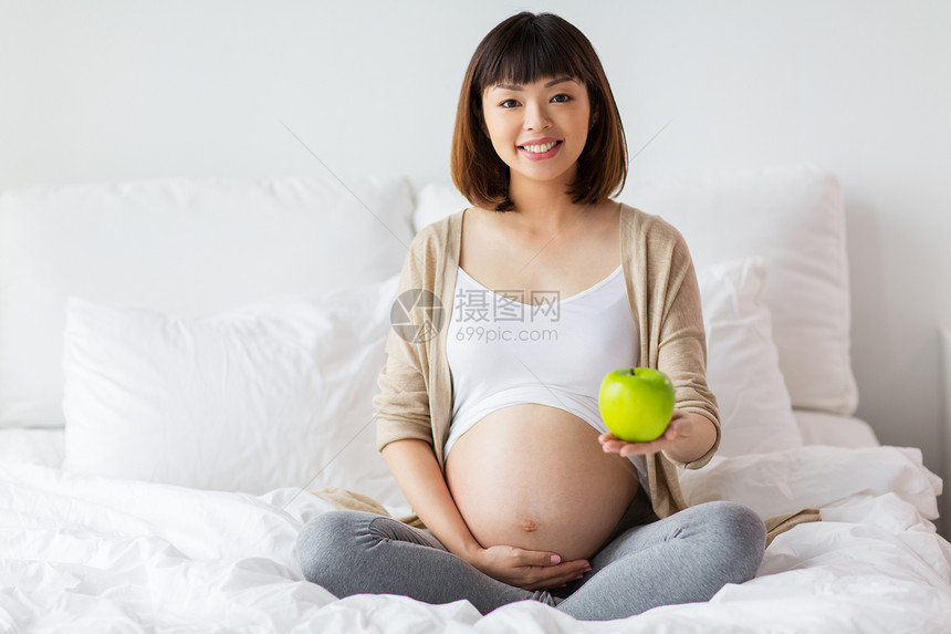 怀孕,人健康的饮食观念快乐的亚洲孕妇坐家里的床上,着绿苹果快乐的孕妇带着苹果家里睡觉图片