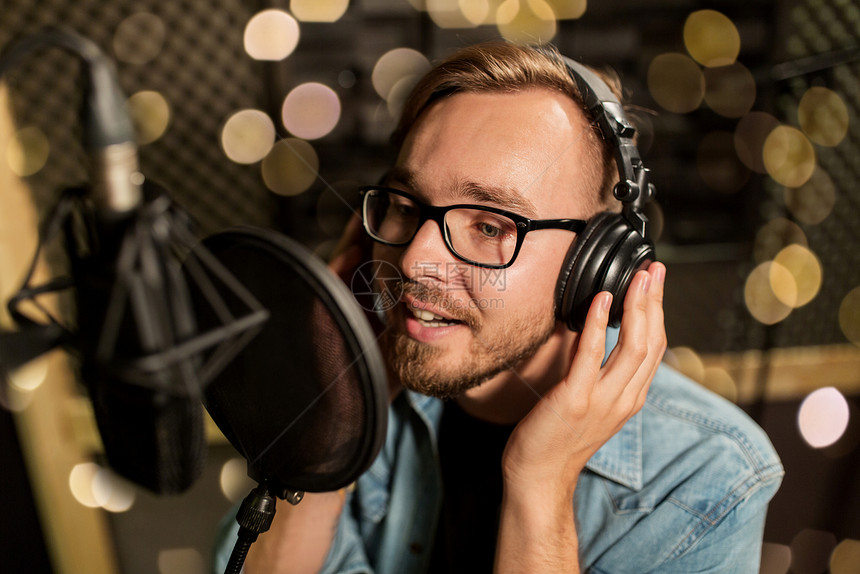 音乐,表演业务,人声音男歌手戴着耳机麦克风节日灯光下的录音棚唱歌带耳机的男人录音棚唱歌图片