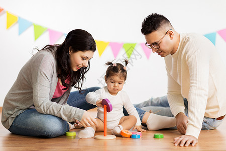 带孩子玩的父亲家庭,假期人的快乐的母亲,父亲小女儿玩环形金字塔婴儿玩具生日聚会上带着父母玩金字塔玩具的女婴带着父母玩金字塔背景