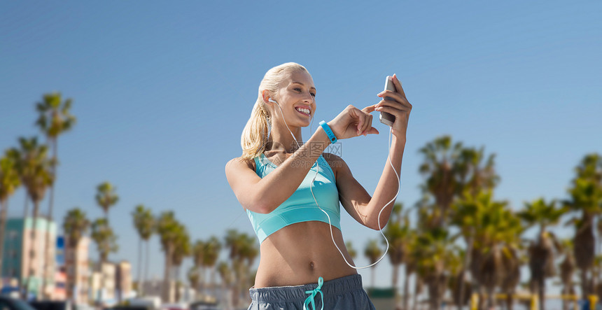 运动,技术健康的生活方式微笑的轻妇女与智能手机,耳机健身跟踪器,听音乐锻炼威尼斯海滩背景加利福尼亚智能手图片