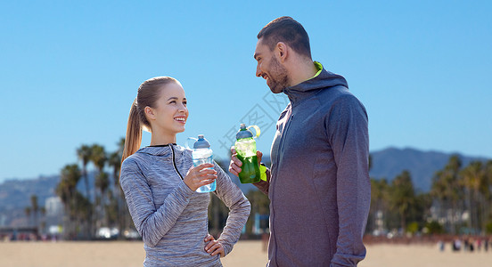 美国减肥素材健身,运动人的微笑夫妇与瓶子的水威尼斯海滩背景加利福尼亚几个运动员威尼斯海滩上喝水几个运动员威尼斯海滩上背景