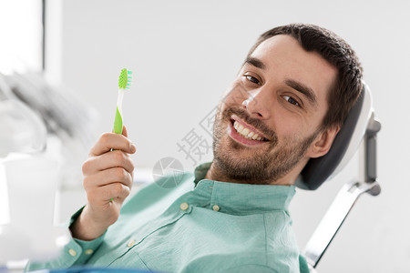 医学,牙科医疗保健快乐的微笑男病人与牙刷椅子上的牙科诊所带牙刷的微笑男人牙科诊所带牙刷的微笑男人牙科诊所背景图片