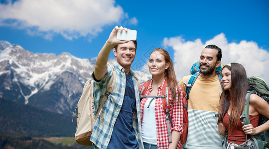 技术,旅游,徒步旅行人们的群微笑的朋友背包阿尔卑斯山背景上用智能手机自拍背包的朋友用智能手机自拍背包旅行高清图片素材