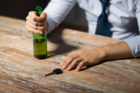 酒后酗酒,醉酒驾驶人的男司机的手与啤酒瓶汽车钥匙桌子上用酒精汽车钥匙把手闭上用酒精汽车钥匙把手闭上背景