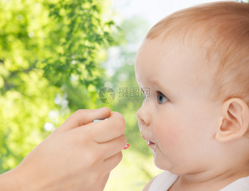 家庭,孩子,饮食父母的母亲的手与勺子喂养小婴儿绿色的自然背景妈妈用勺子喂小宝宝的手图片