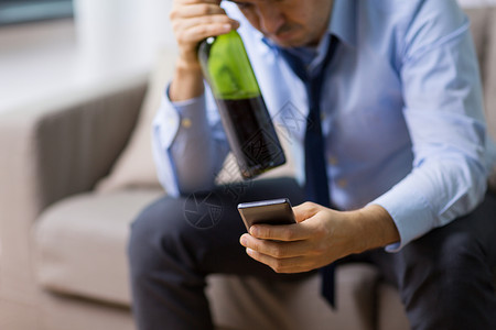 酗酒,酒精家里用智能手机瓶酒接近喝醉的人家里智能手机瓶酒精的男人背景图片