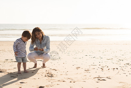 轻的母亲蹒跚学步的孩子探索海滩图片