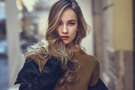 城市背景的金发女人漂亮的轻女孩穿着黑色皮夹克迷你裙站街上漂亮的俄罗斯女,留着长长的波浪发型蓝色的眼睛背景图片