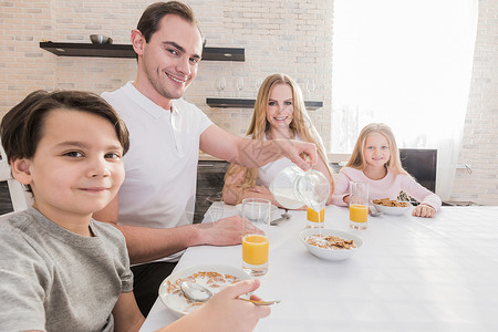 快乐的轻父母他们的孩子坐厨房的桌子上,吃薄片,吃健康的早餐,享受早上好,友好的关系家庭饮食观念家庭吃早餐背景图片