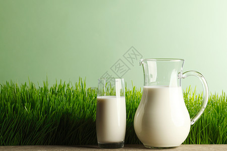 新鲜草地背景上的杯牛奶罐子图片