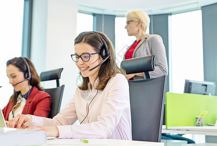 女客户服务代表用耳机,而同事办公室背景图片