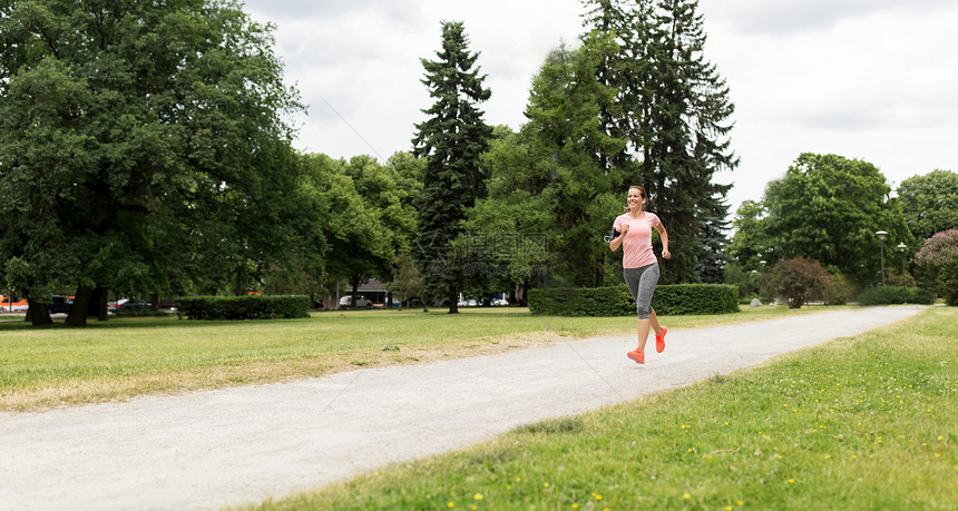 健身,运动健康的生活方式微笑的女人带着耳机公园跑步听音乐耳机的女人公园跑图片