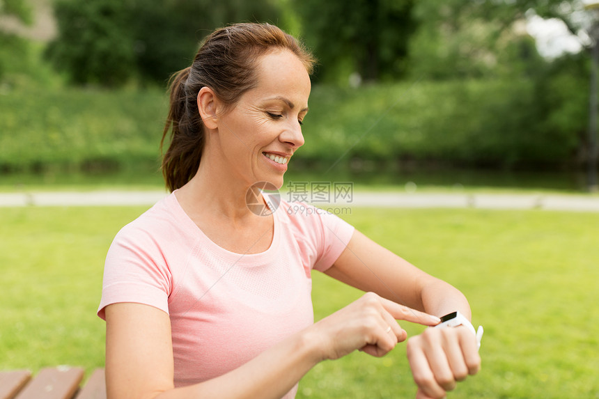 运动技术微笑的女人与智能手表健身跟踪器公园公园里智能手表健身追踪器的女人图片