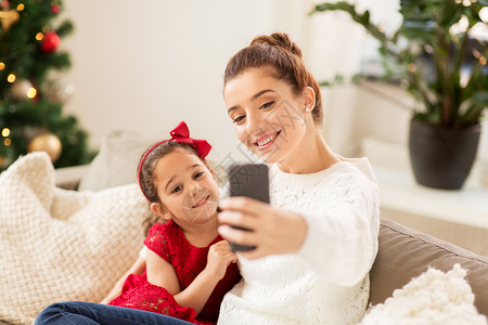 诞节,技术家庭快乐的母亲小女儿家里用智能手机自拍家人家用智能手机自拍图片