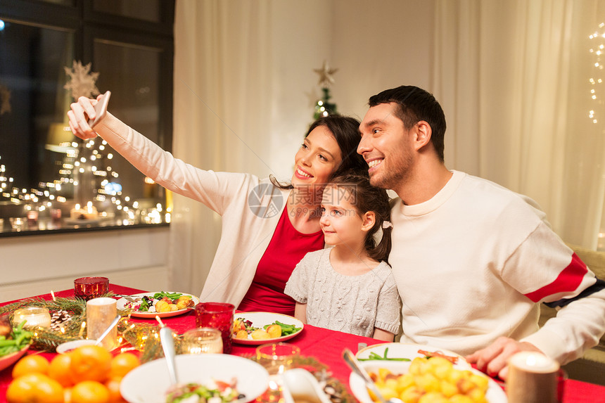 假期,家庭庆祝快乐的母亲,父亲小女儿吃诞晚餐,并家里用智能手机自拍快乐的家人诞晚餐上自拍图片