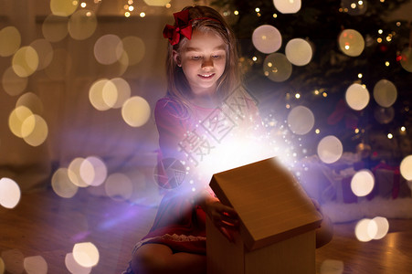 诞节,假期童的快乐的小女孩打开礼品盒与魔法灯黑暗中家里微笑的女孩晚上打开诞礼物背景图片