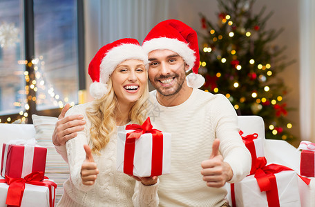 节日人们的幸福的夫妇戴着诞老人的帽子,礼品盒家里的诞树灯光背景上竖大拇指诞礼物竖大拇指的幸福夫妇背景图片