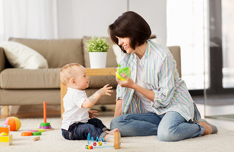 儿童防骗家庭,孩子母亲的快乐的母亲与小儿子家里玩发育玩具小杯子快乐的母亲家里给小儿子喝西皮杯背景