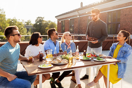 休闲人们的快乐的聚会主持人提供肉给他的朋友烧烤聚会屋顶夏天夏天屋顶的烧烤派上的朋友背景图片