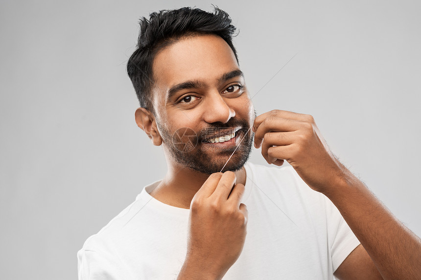 口腔护理,卫生人的微笑的轻印度男子牙线清洁牙齿灰色背景印度男人用牙线清洁牙齿图片
