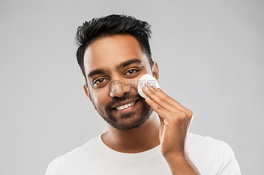 美容,皮肤护理人的微笑的轻印度男子清洁他的脸与棉垫灰色的背景微笑的印度男人用棉垫洗脸图片