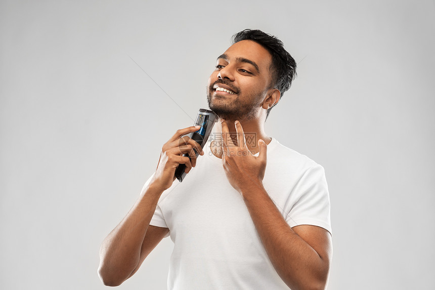 美容,技术人的微笑的印度男子剃须胡须与修剪灰色背景微笑的印度男人用修剪器刮胡子图片