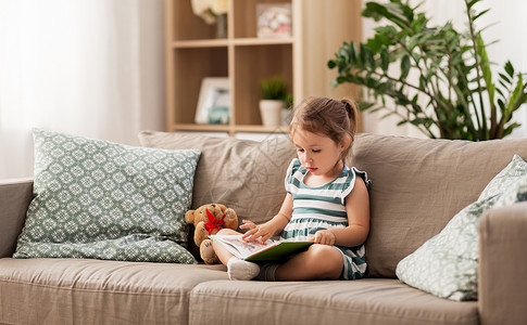 童人的小女孩坐沙发上看书,玩具泰迪熊家小女孩家看书高清图片