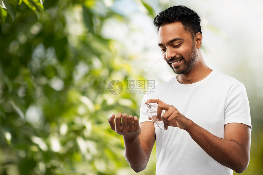 男香水,美容人的快乐微笑的轻印度男子喷香水他的手腕上绿色的自然背景印度男人香水自然背景图片
