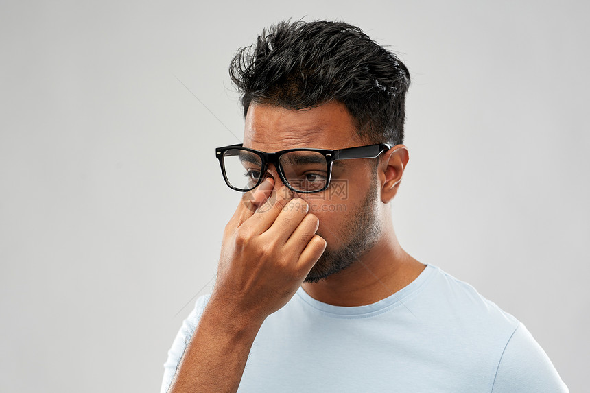 人,视觉过度工作的疲惫的印度男子戴着眼镜,灰色背景上摩擦鼻梁疲惫的印度男人戴着眼镜,擦着鼻梁图片